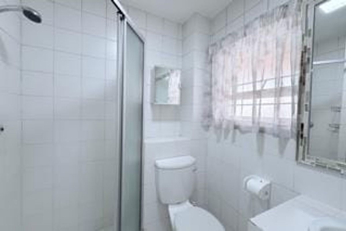 A functional bathroom featuring a shower enclosure, toilet, and vanity basin with wall-mounted mirror, finished with clean white wall tiling.