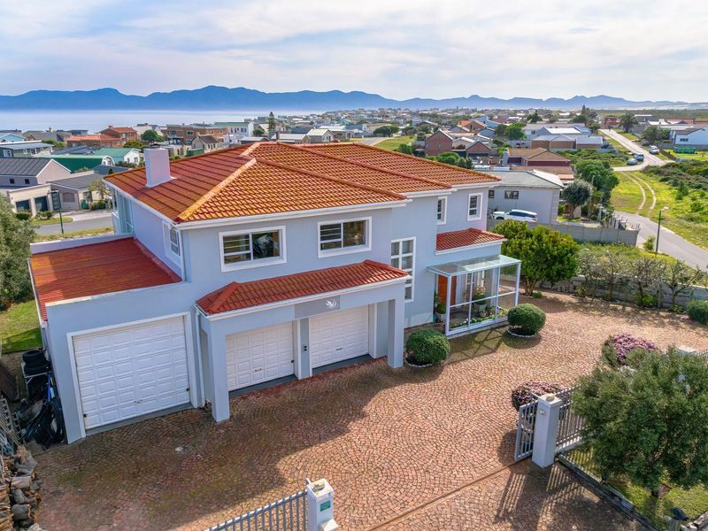 Aerial view of a double-story residential property featuring a terracotta tiled roof, triple garage, and paved driveway in a coastal neighborhood setting.