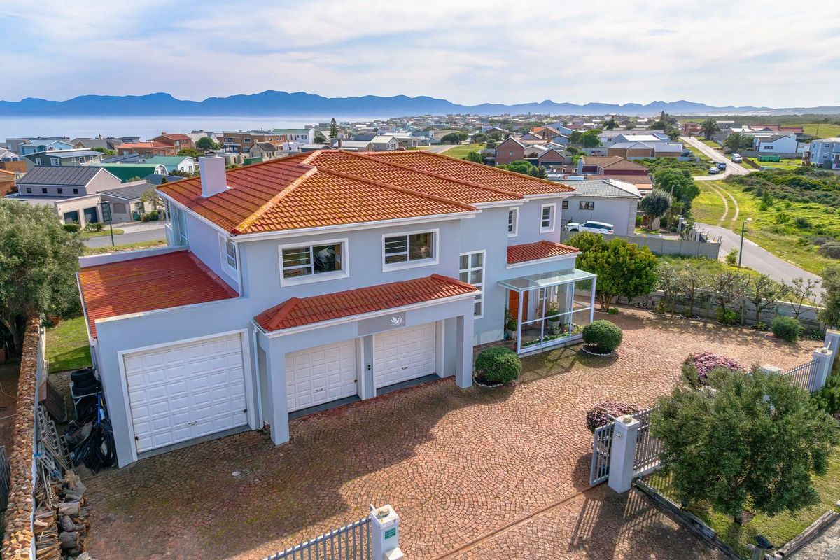 Aerial view of a double-story residential property featuring a terracotta tiled roof, triple garage, and paved driveway in a coastal neighborhood setting.