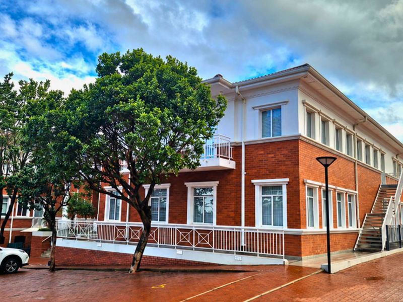 A well-maintained office building featuring a classic red brick facade, white trim, and an external staircase, set within a paved professional complex.