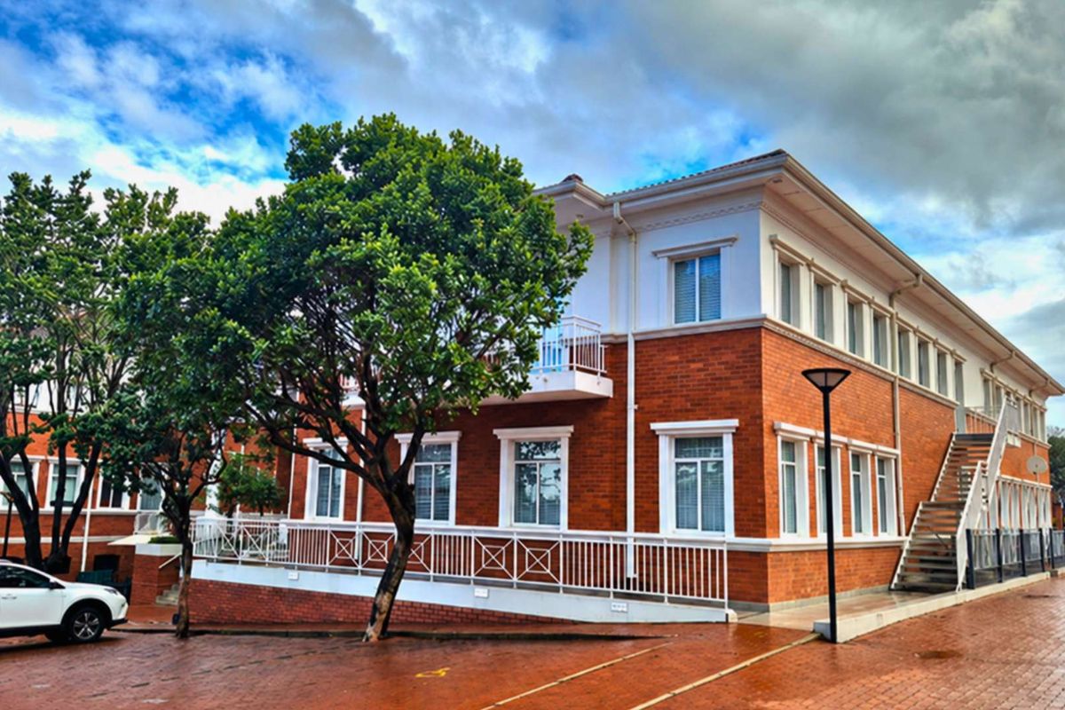 A well-maintained office building featuring a classic red brick facade, white trim, and an external staircase, set within a paved professional complex.