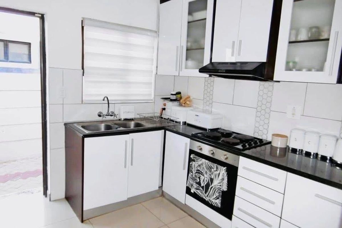 A modern kitchen featuring white cabinetry, black countertops, a built-in oven, hob, extractor fan, and a double sink with tiled splashbacks.