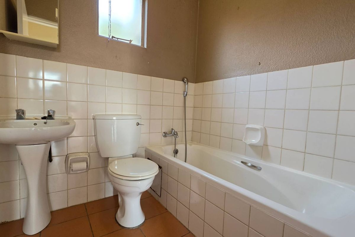A dated bathroom featuring a pedestal sink, standard toilet, and a bathtub with a handheld shower attachment, finished with white wall tiles.