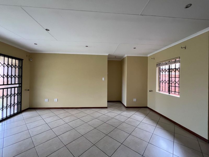 A spacious, empty living area featuring neutral walls, tiled flooring, recessed lighting, and security fixtures on the windows and doors.