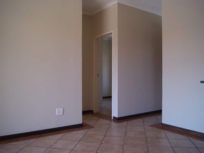A clean, empty hallway featuring neutral wall tones and tiled flooring, providing access to adjacent rooms within the apartment.