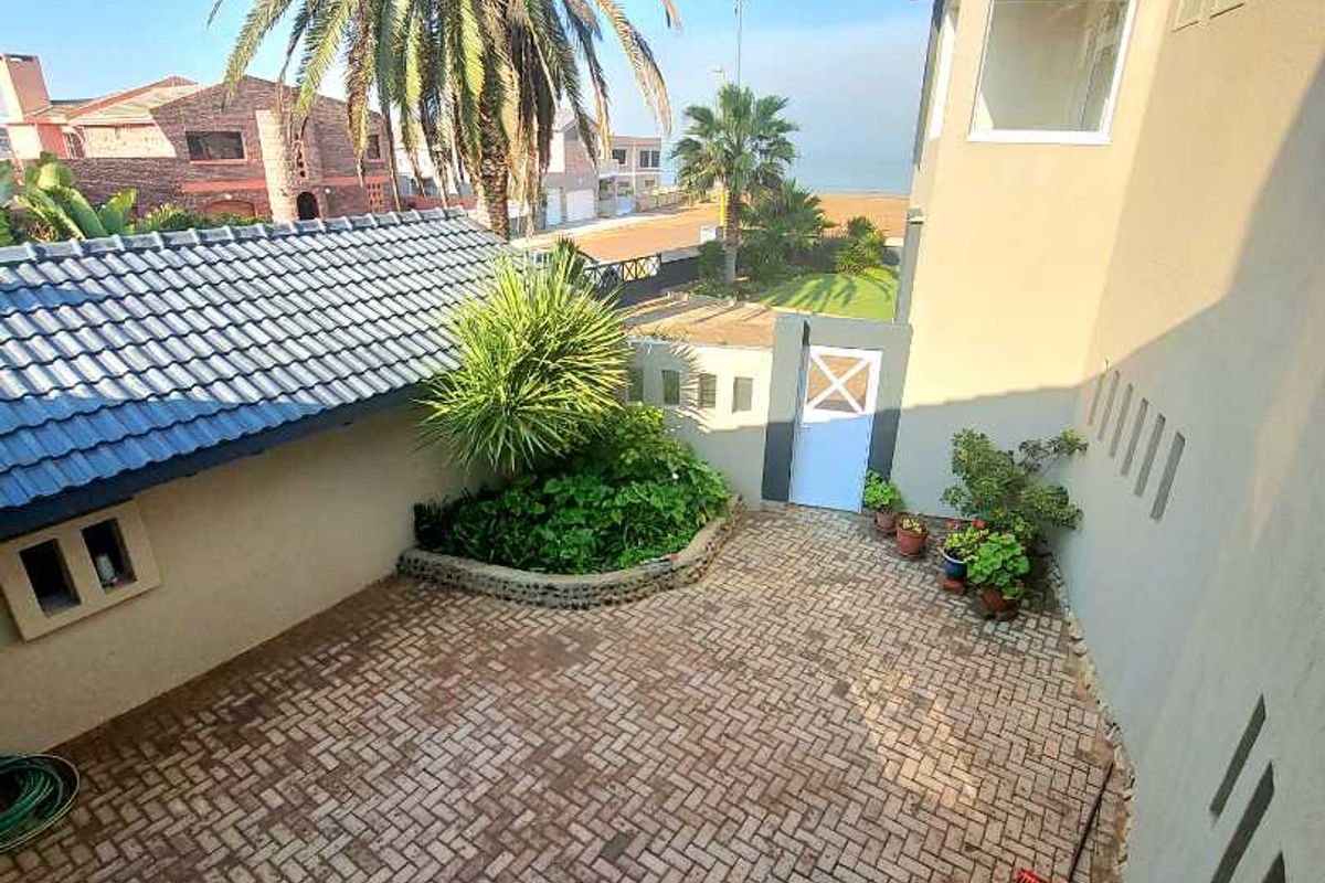 A private rear courtyard featuring brick paving, a raised garden bed, and a secure pedestrian gate leading towards the coastal area.