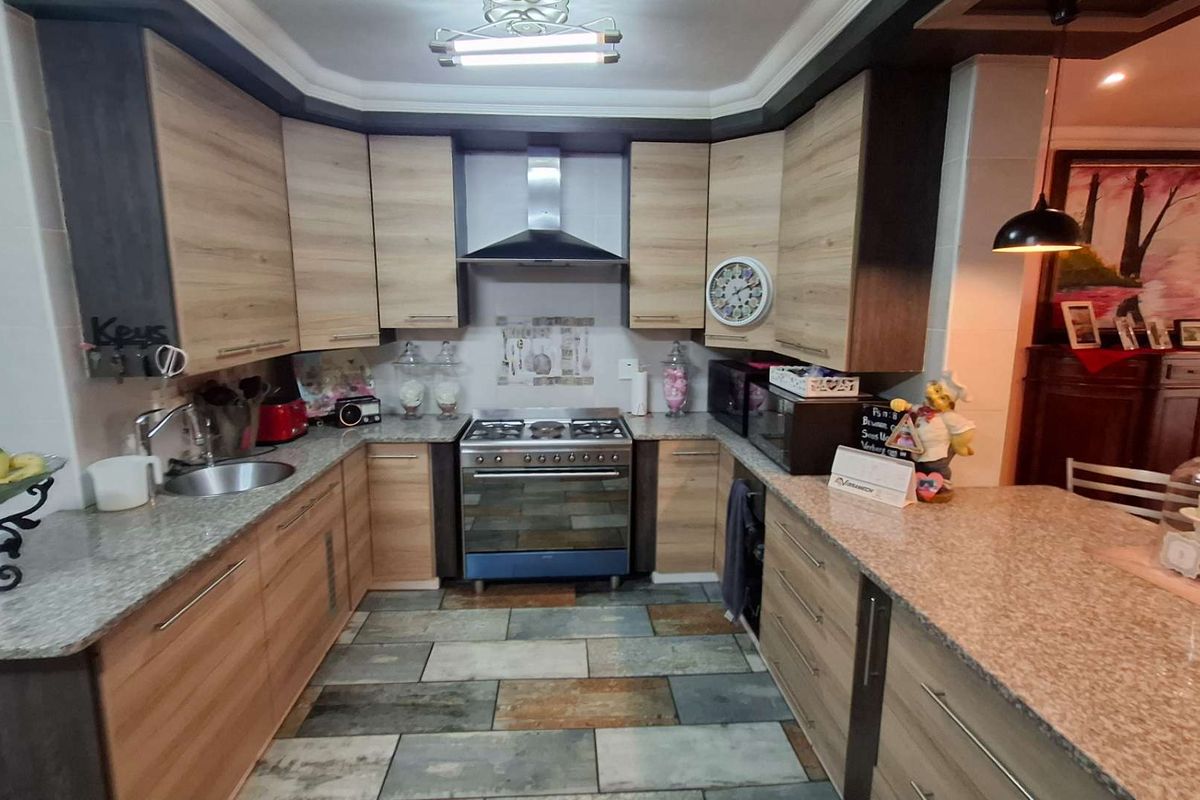 Modern kitchen featuring wood-finish cabinetry, granite countertops, stainless steel appliances, and durable stone tile flooring.
