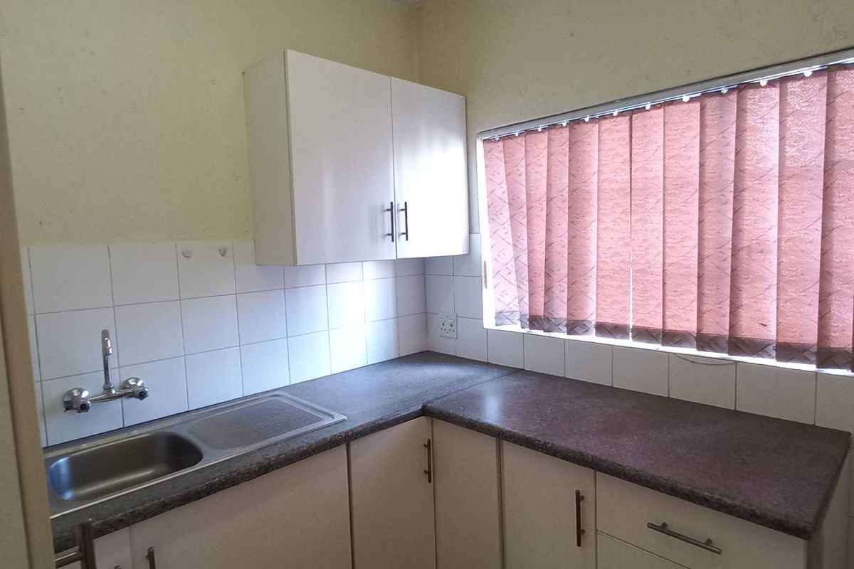A functional kitchen area featuring built-in cabinetry, laminate countertops, a stainless steel sink, and tiled splashbacks, ready for modernization.