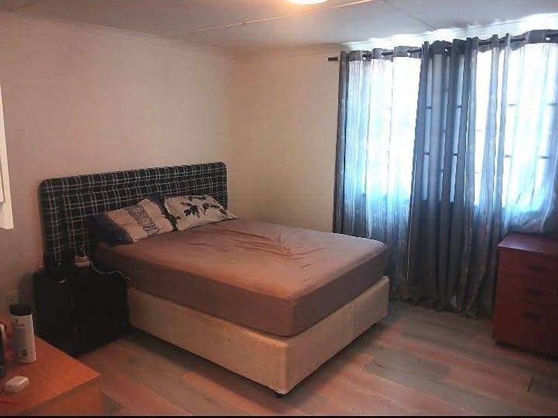 A standard bedroom featuring laminate flooring and window treatments, providing a functional space for rest.