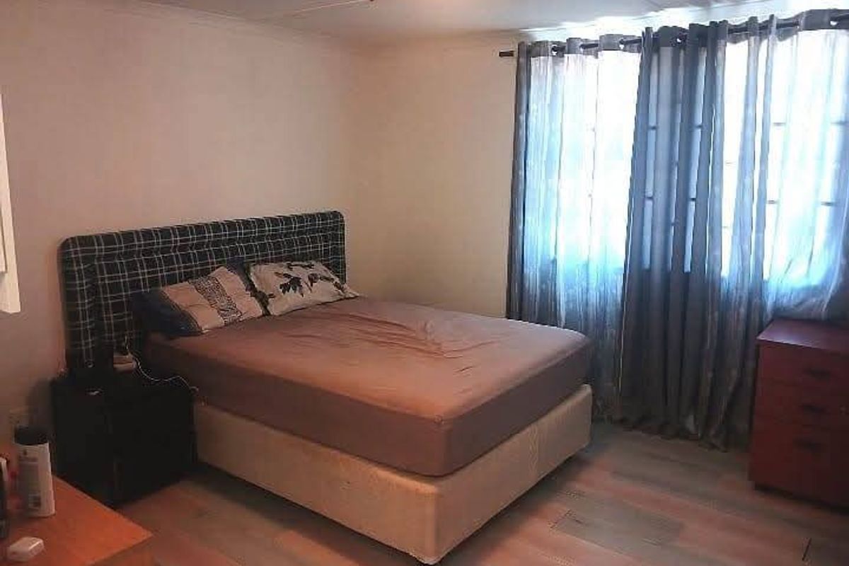 A standard bedroom featuring laminate flooring and window treatments, providing a functional space for rest.