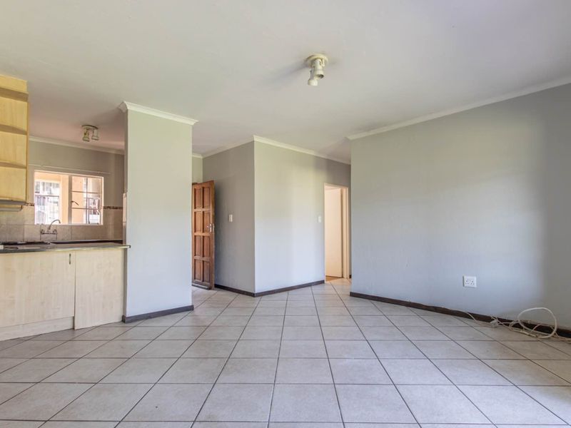 Open-plan living area featuring tiled flooring and a compact kitchen with built-in cabinetry, offering a blank canvas for interior design.