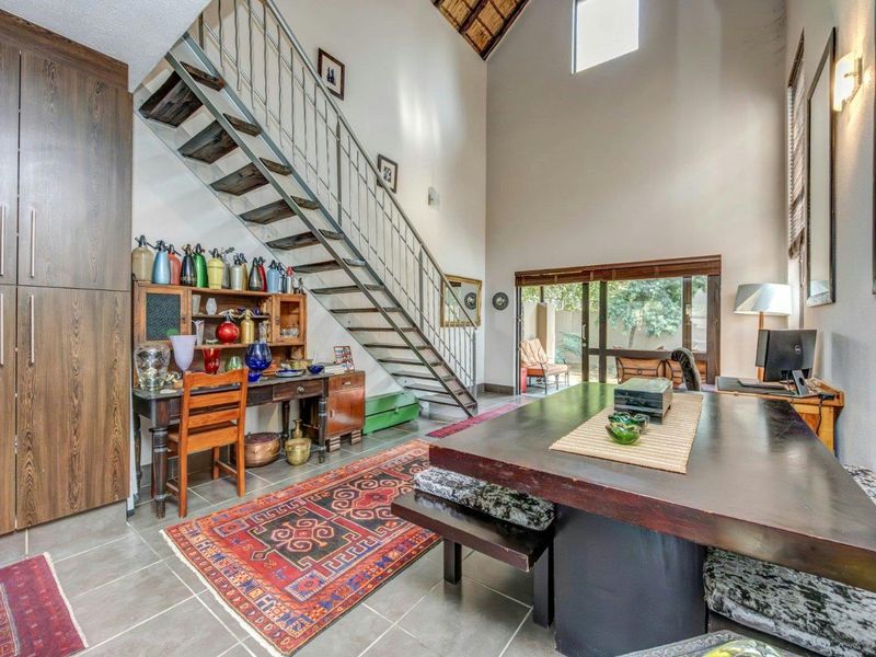 Spacious open-plan living area featuring double volume ceilings, a modern metal staircase, tiled flooring, and large sliding doors leading to the outdoor patio.