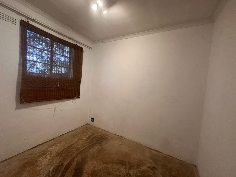 An empty bedroom featuring plain white walls, a window with security bars, and an unfinished floor surface, ready for renovation or flooring installation.