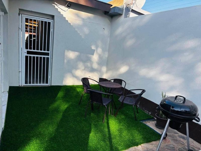 A compact outdoor patio area featuring artificial turf, a secure entrance gate, and high boundary walls for privacy.