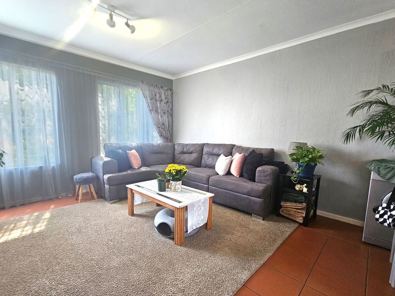 A spacious living room featuring tiled flooring, neutral grey walls, and large windows that provide ample natural light.