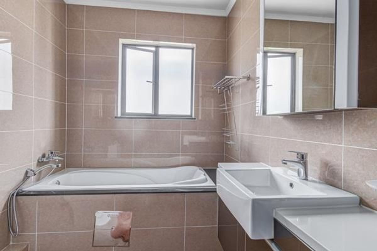 A modern bathroom featuring floor-to-ceiling tiled walls, a built-in bathtub with shower mixer, and a contemporary wall-mounted vanity basin.