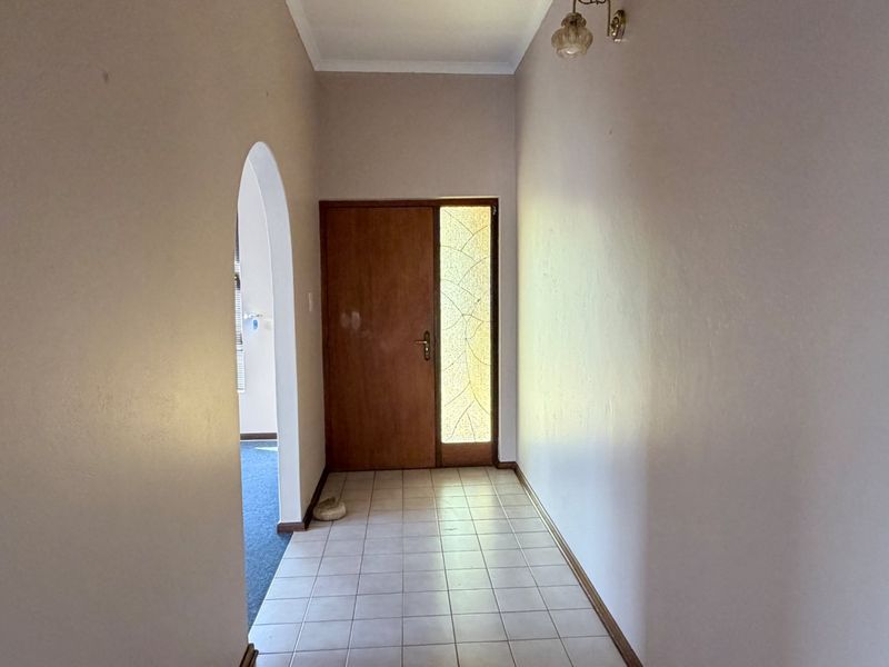 A bright entrance hall featuring tiled flooring, a classic arched doorway leading to adjacent living spaces, and a timber front door with a decorative sidelight.