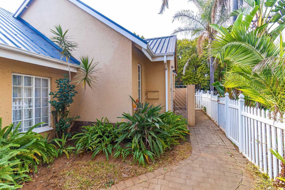 A view of the townhouse rear exterior featuring a paved walkway, white picket fencing, and metal roofing.