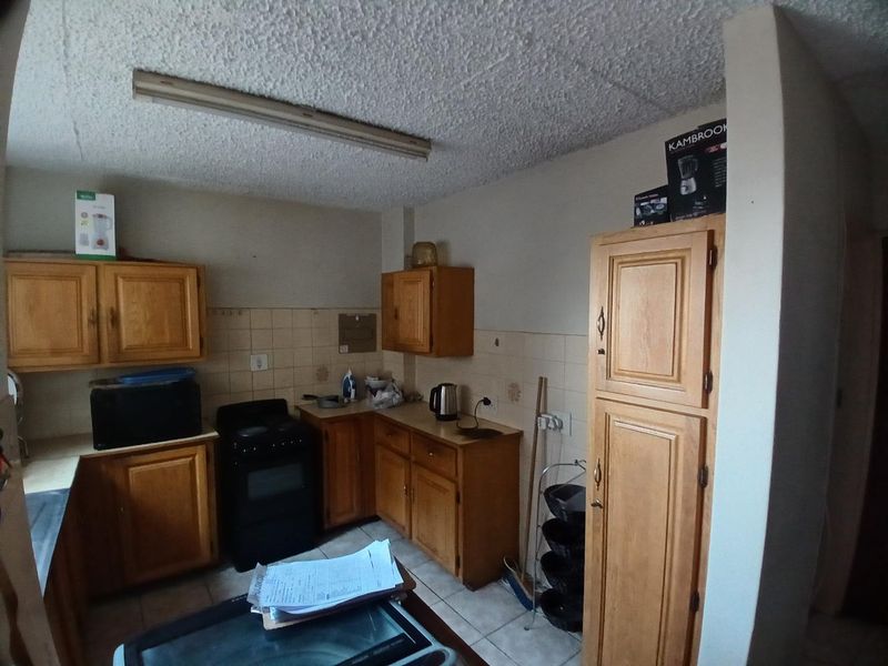 A dated kitchen featuring wooden cabinetry, tiled backsplash, and a freestanding stove, offering potential for modernization and renovation.