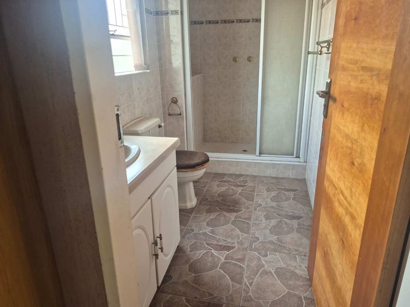 A functional bathroom featuring a vanity cabinet, toilet, and a separate shower enclosure with tiled walls and flooring.