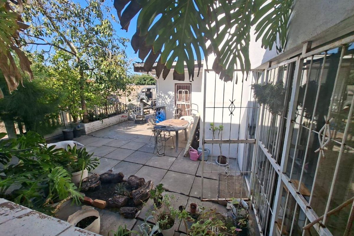 A paved rear courtyard area featuring a metal security gate, established garden beds, and direct access to the main dwelling.