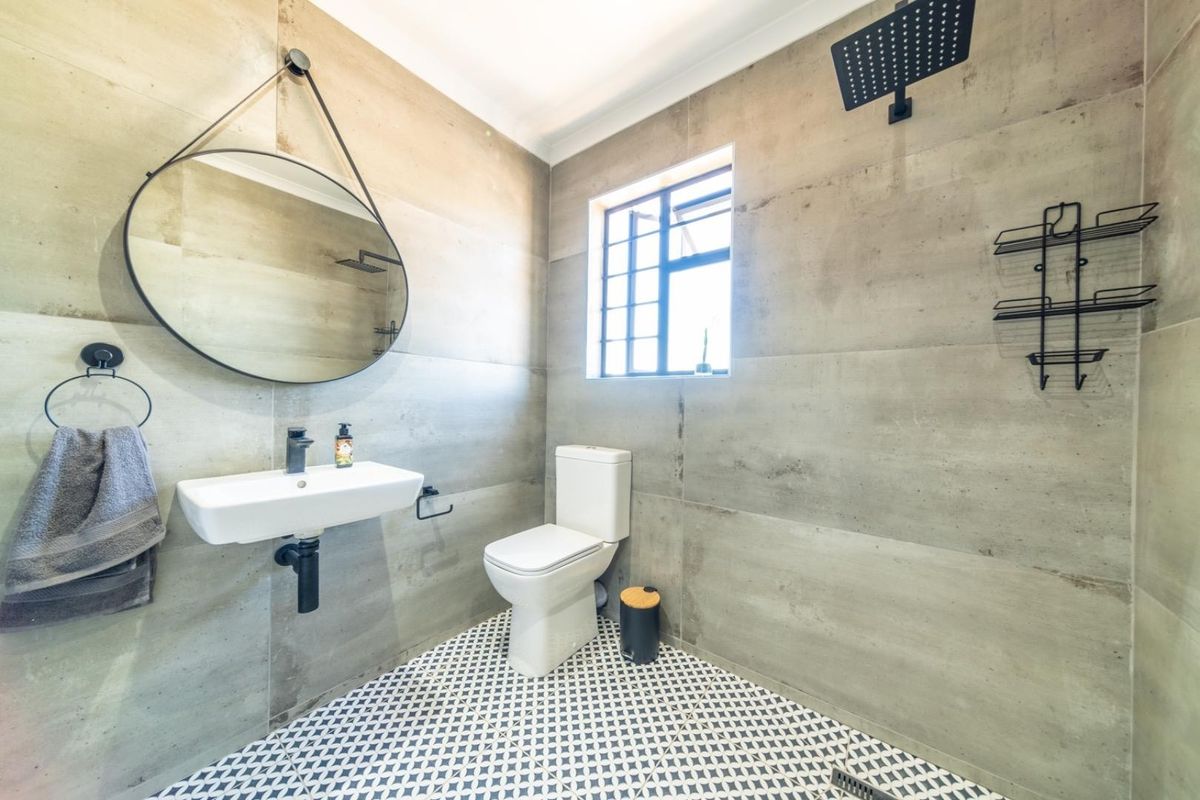 Modern bathroom featuring large-format concrete-look wall tiles, patterned floor tiles, a wall-mounted basin, and a rainfall shower head.
