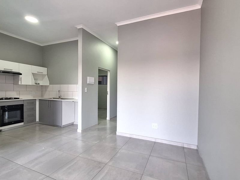 Modern open-plan kitchen and living area featuring neutral grey tones, tiled flooring, and built-in cabinetry with integrated oven and hob.