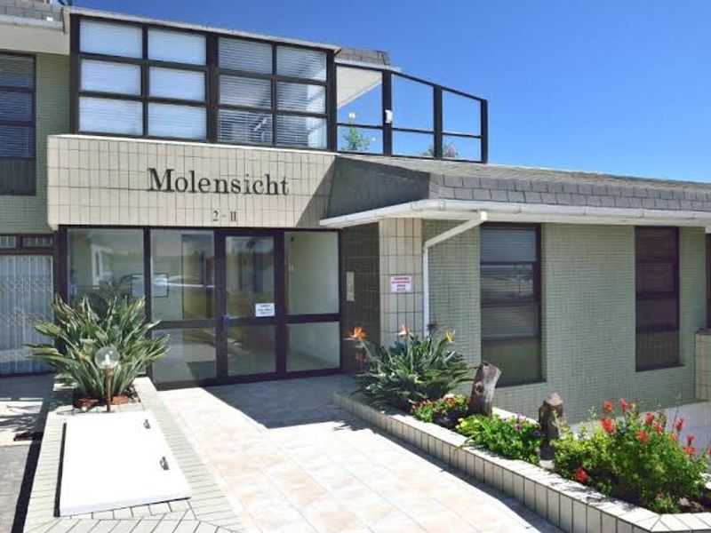 Front entrance view of Molensicht apartment complex featuring a tiled facade, glass entry doors, and landscaped garden beds.