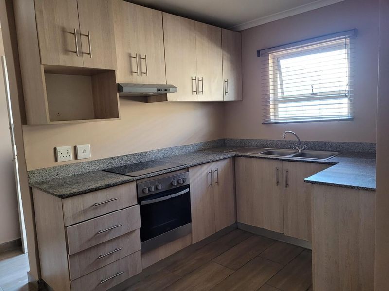A clean and functional kitchen featuring light wood-tone cabinetry, granite countertops, integrated oven and hob, and a double-basin stainless steel sink.