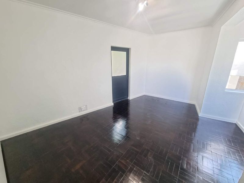 An empty living room featuring polished dark parquet flooring, white walls, and a single door leading to an adjacent space.
