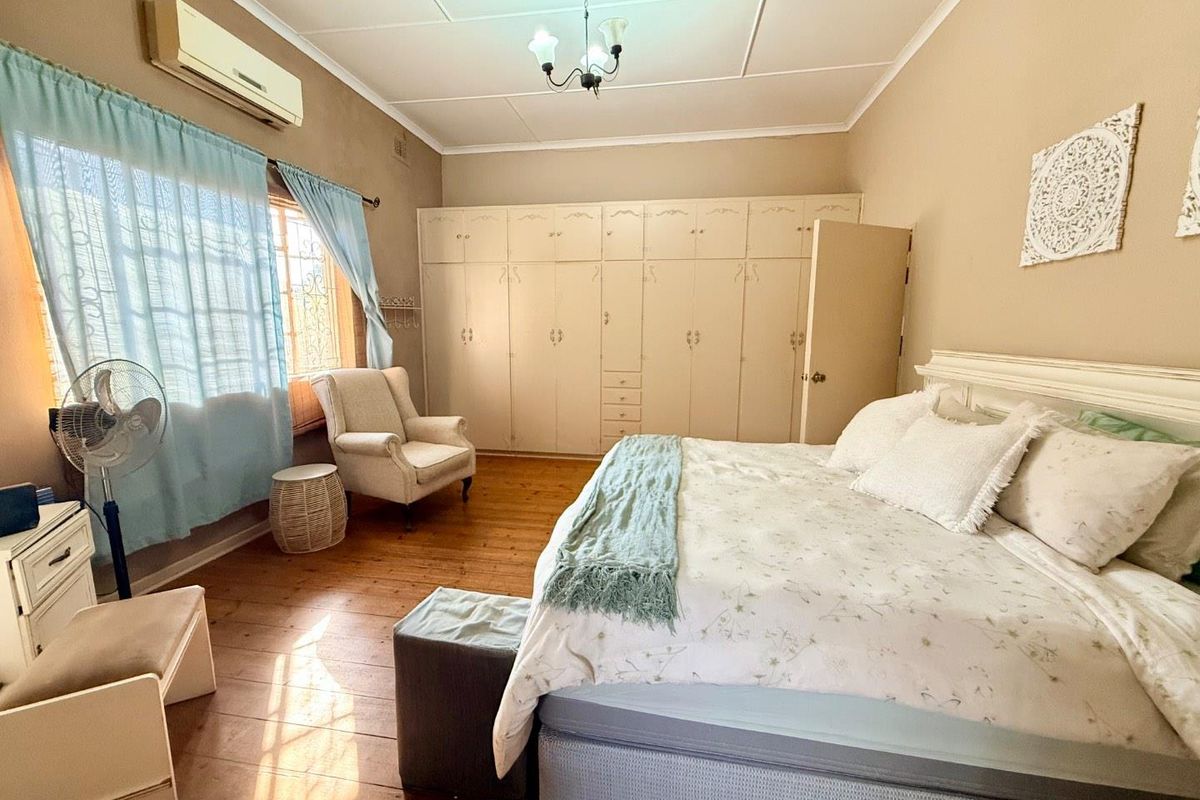 Spacious bedroom featuring extensive built-in cabinetry, polished timber flooring, and a wall-mounted air conditioning unit.