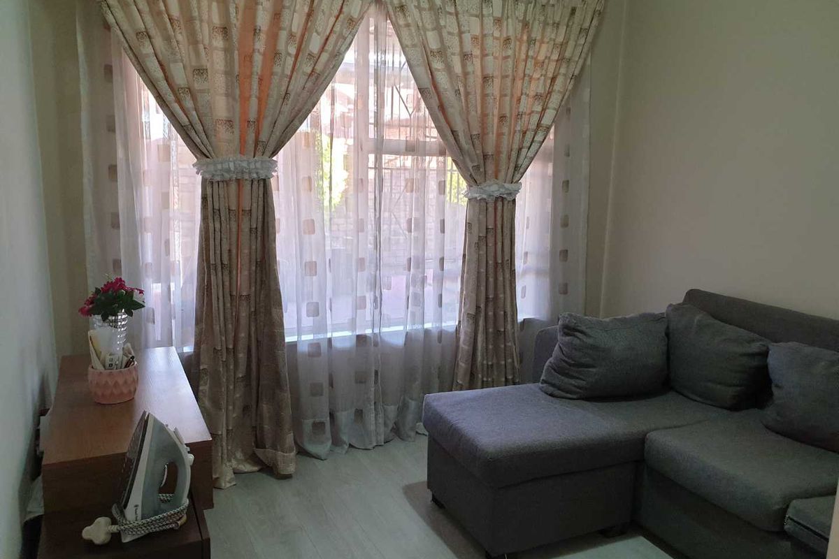 A living room area featuring light-toned laminate flooring and large windows dressed with curtains.