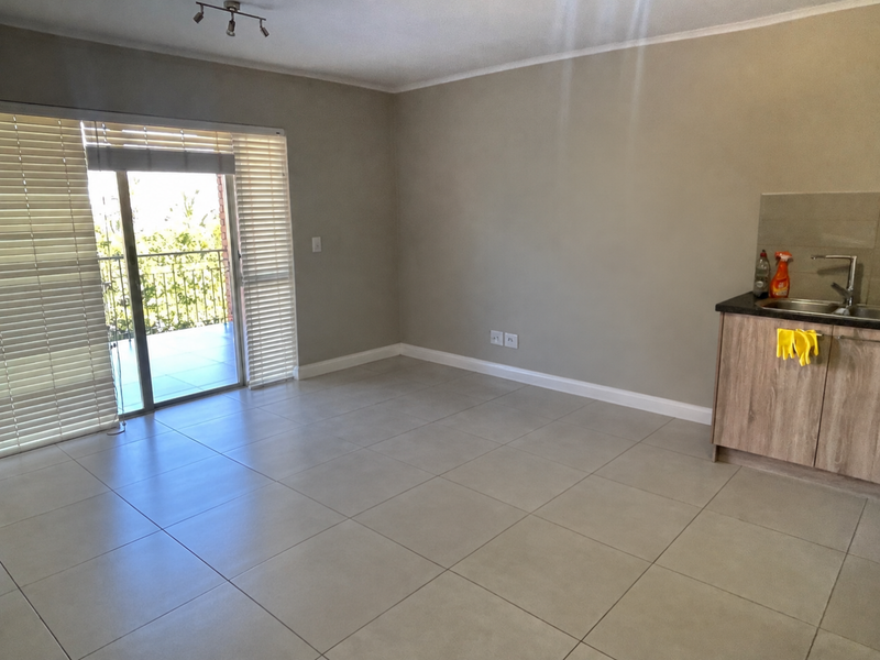 An open-plan living area featuring neutral tiled flooring, a kitchenette with built-in cabinetry, and a sliding glass door leading to a balcony.