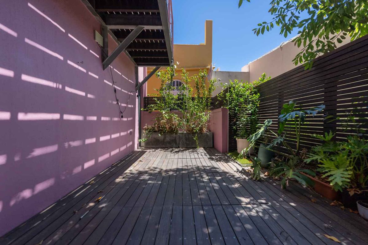 A private rear courtyard featuring timber decking, perimeter slat fencing, and built-in concrete planter boxes, accessible via an external staircase.