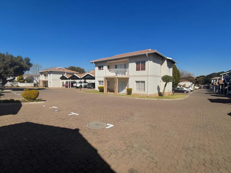 Exterior view of a multi-unit apartment complex featuring paved parking areas, carports, and residential buildings with tiled roofs and balconies.