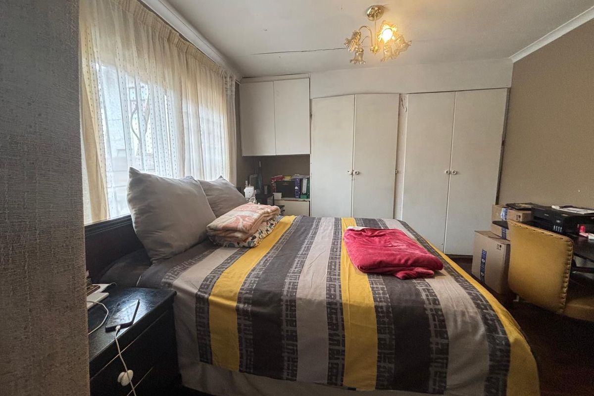 A bedroom featuring built-in cupboards, a ceiling light fixture, and large windows with curtains, providing a functional living space.