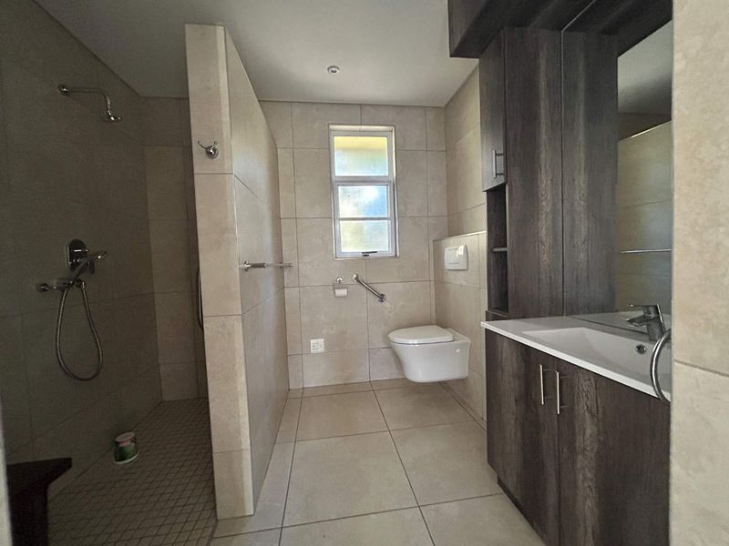 Modern bathroom featuring a walk-in shower, wall-hung toilet, and a dark wood vanity cabinet with integrated basin, finished with neutral floor-to-ceiling tiles.