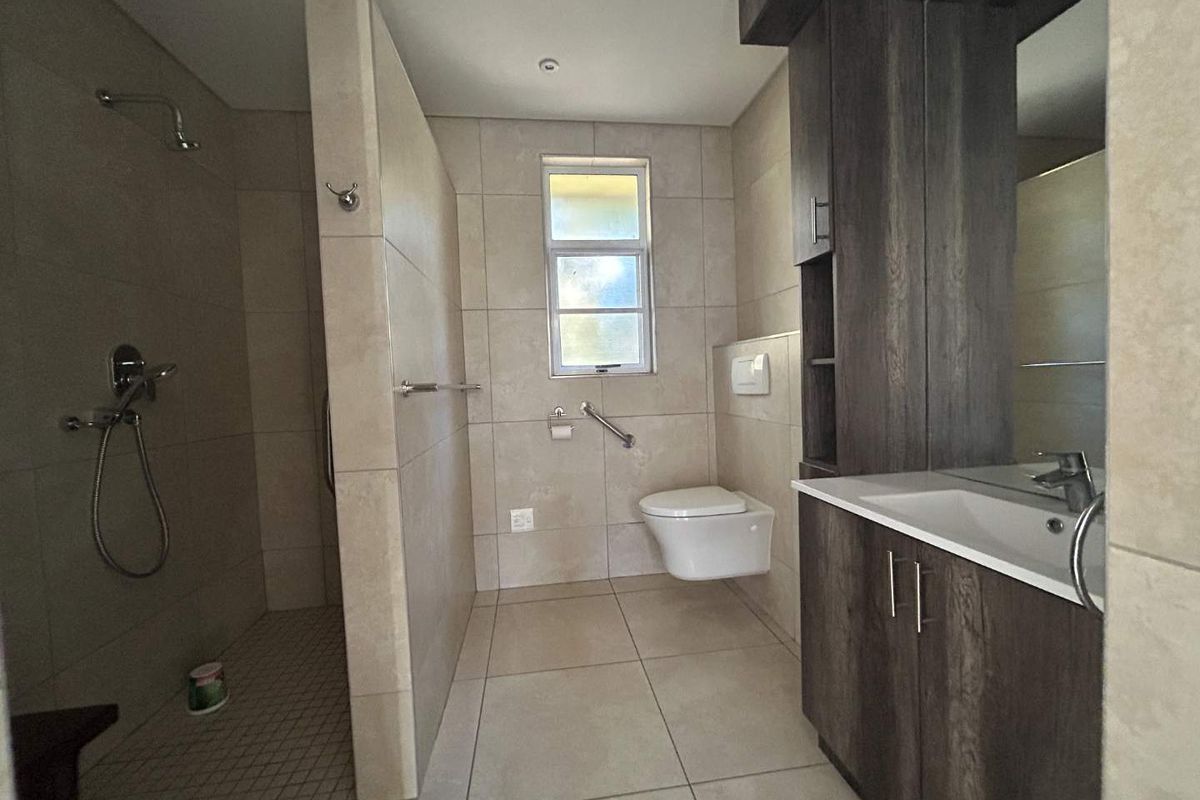 Modern bathroom featuring a walk-in shower, wall-hung toilet, and a dark wood vanity cabinet with integrated basin, finished with neutral floor-to-ceiling tiles.