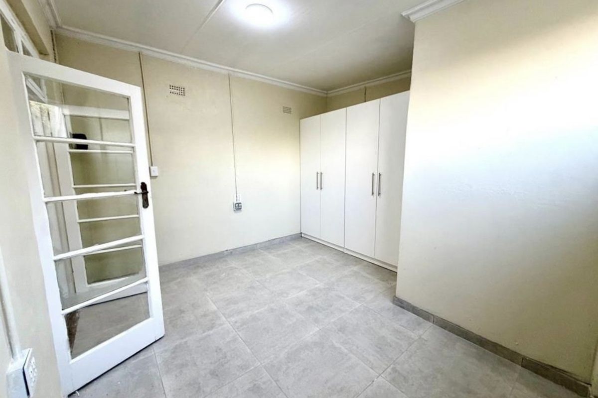 A clean, empty bedroom featuring neutral tiled flooring, built-in cupboards, and a classic glass-panelled door, offering a versatile space ready for personalization.
