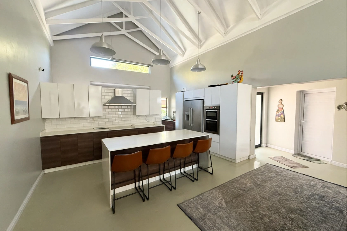 Modern kitchen featuring a high vaulted ceiling with exposed trusses, a central island, subway tile backsplash, and sleek built-in cabinetry.