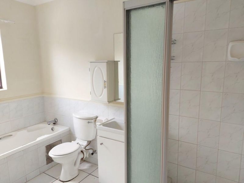A functional bathroom featuring a built-in bathtub, separate shower enclosure, toilet, and vanity cabinet with neutral tiled finishes.