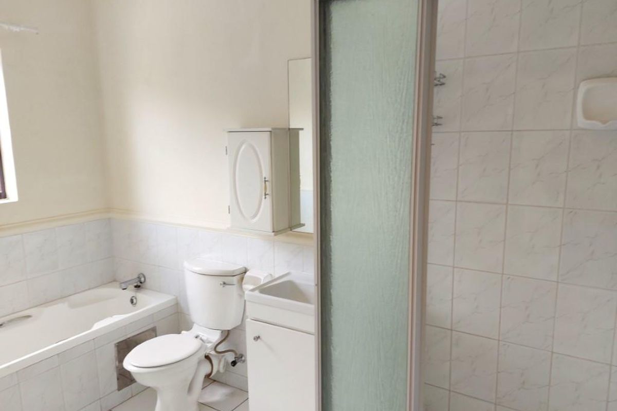 A functional bathroom featuring a built-in bathtub, separate shower enclosure, toilet, and vanity cabinet with neutral tiled finishes.