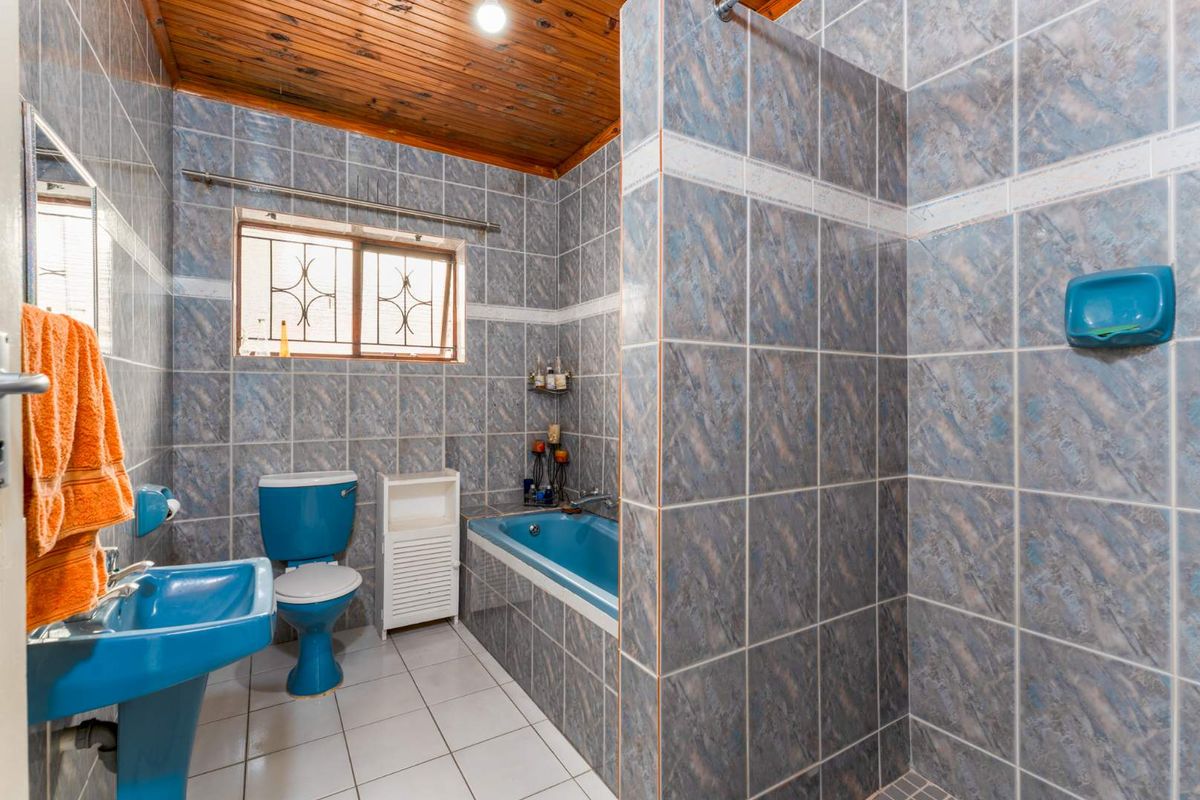 A dated bathroom featuring blue sanitaryware, a built-in bathtub, a separate shower enclosure, and a timber-clad ceiling.
