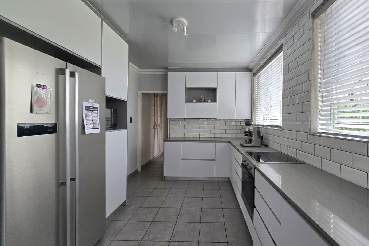 Modern kitchen featuring white cabinetry, subway tile backsplash, stone countertops, integrated oven, and hob, complemented by neutral floor tiling and ample natural light.
