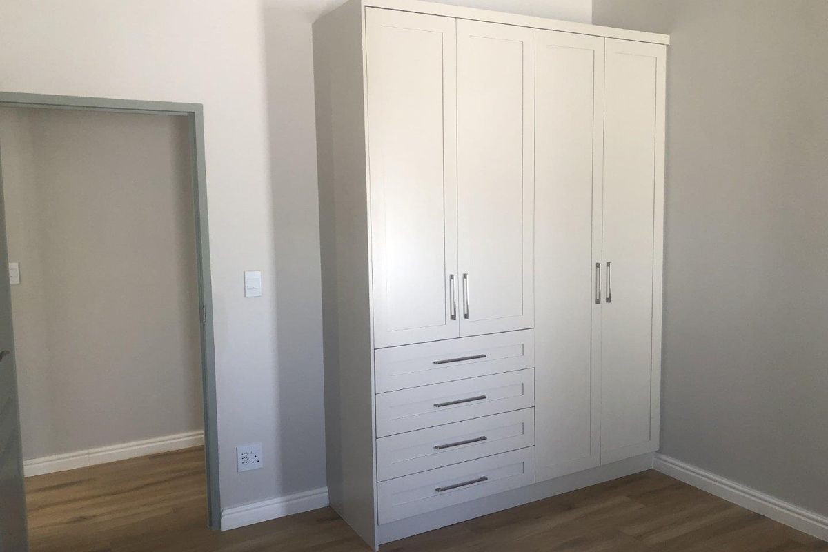 A bedroom featuring a modern, white built-in wardrobe with integrated drawers and light wood-look flooring.