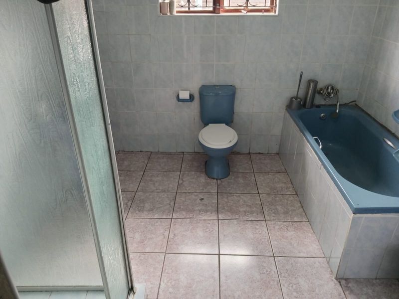 A dated bathroom featuring a blue bathtub, matching toilet, and a separate shower enclosure with tiled finishes throughout.
