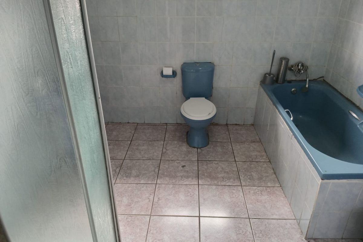 A dated bathroom featuring a blue bathtub, matching toilet, and a separate shower enclosure with tiled finishes throughout.
