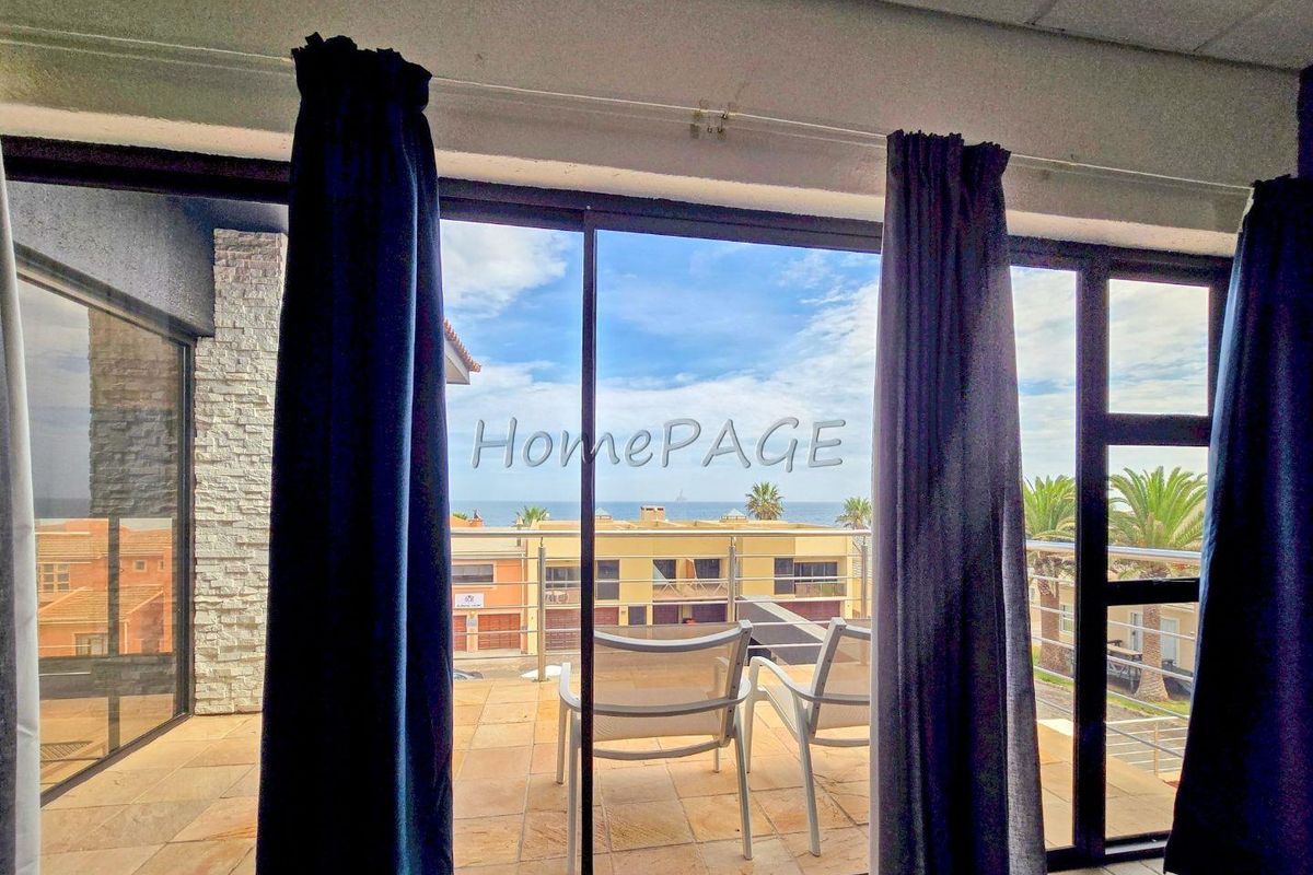 A bright living area featuring large sliding glass doors that open onto a tiled balcony with scenic coastal views.