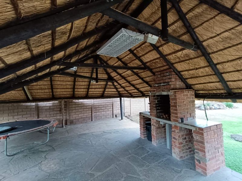 Covered outdoor patio area featuring a traditional thatched roof, exposed timber beams, and a built-in brick braai, perfect for outdoor entertaining.