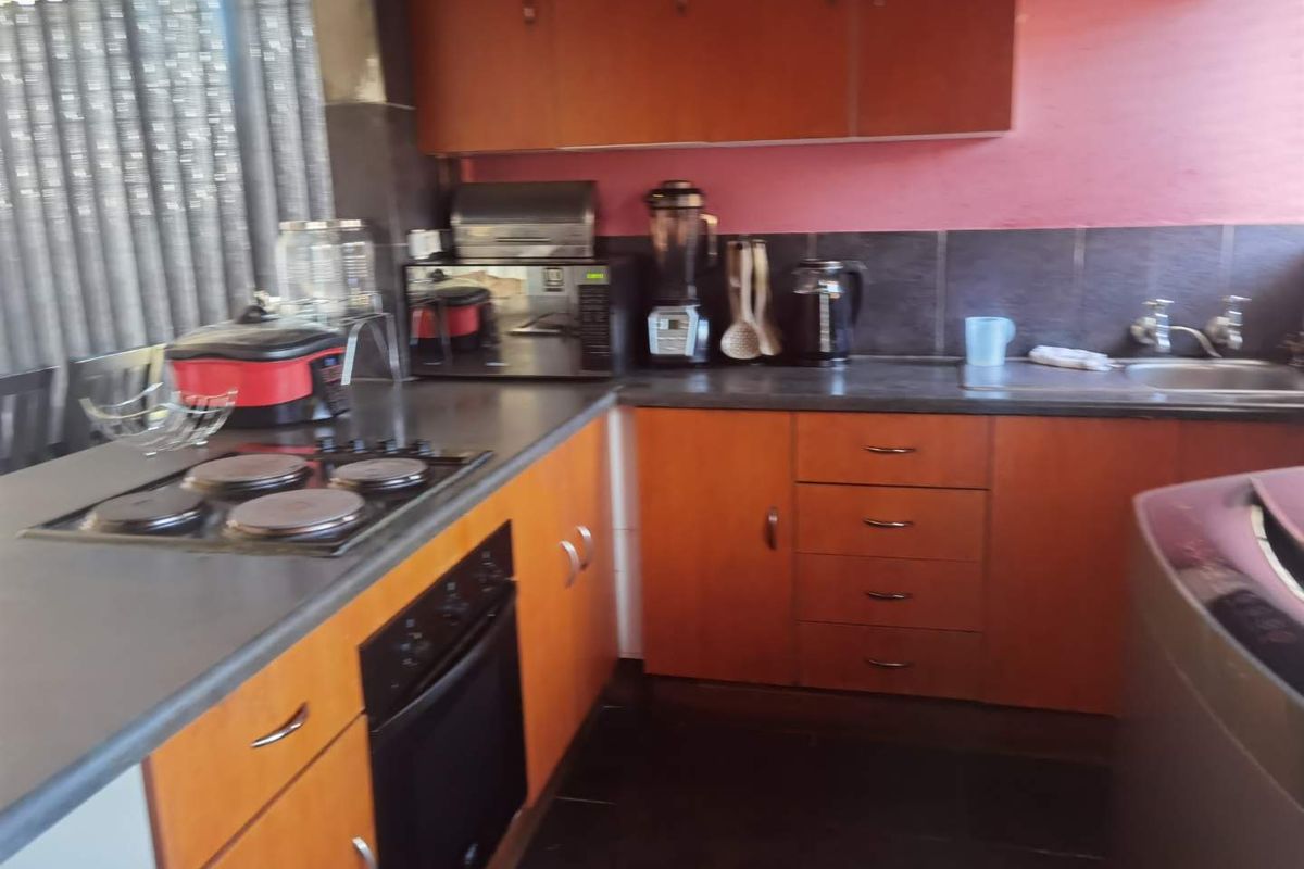 A functional kitchen featuring wooden cabinetry, dark laminate countertops, an integrated electric hob and oven, and a stainless steel sink with tiled backsplash.